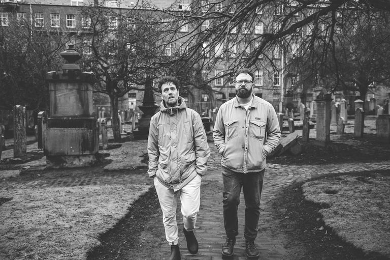 Ben Ottewell and Ian Ball from Gomez walking through a historic graveyard in a black-and-white portrait.